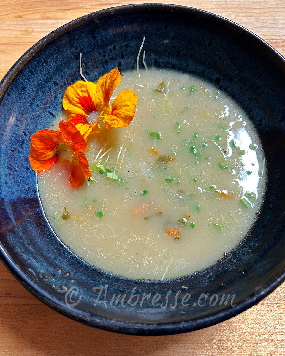 Bresse soup, with potatoes, cabbage, and microgreens, garnished with spicy edible nasturtium flowers.